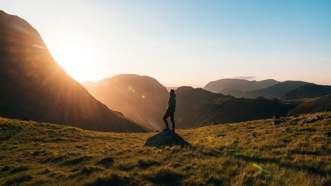 Person steht bei Sonnenaufgang auf einem Felsen in den Bergen