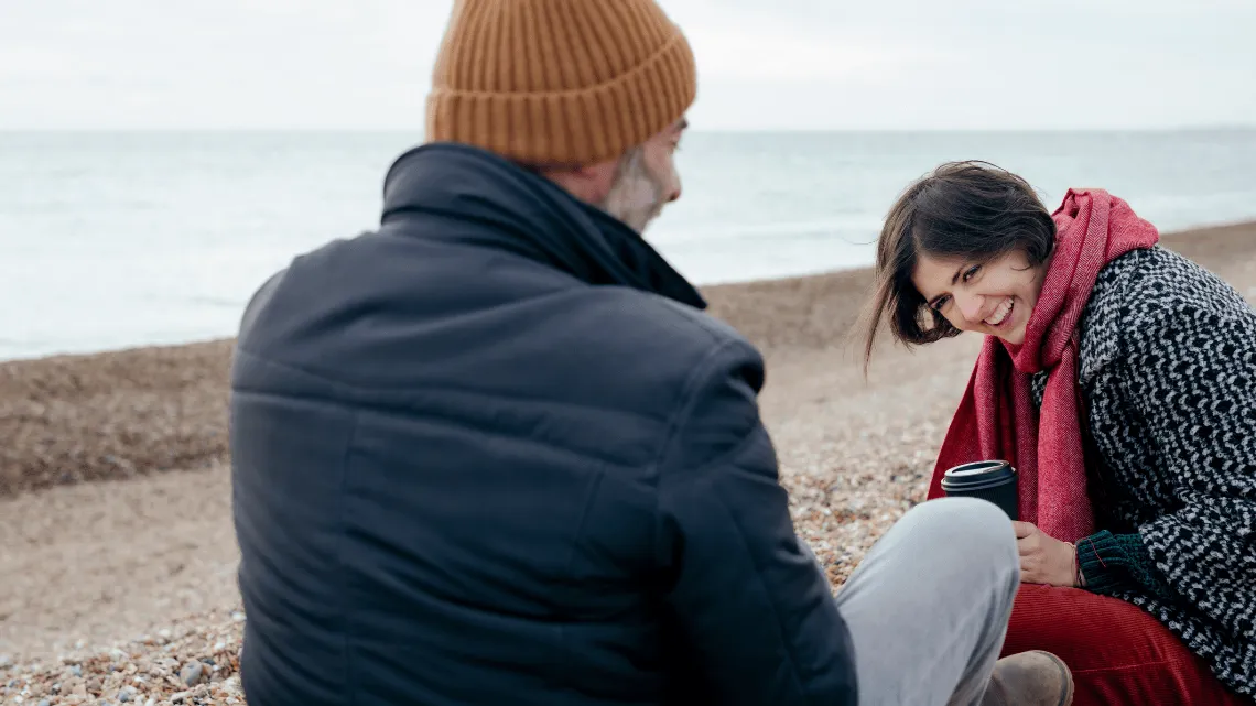 Zwei Menschen sitzen an einem Kiesstrand und unterhalten sich